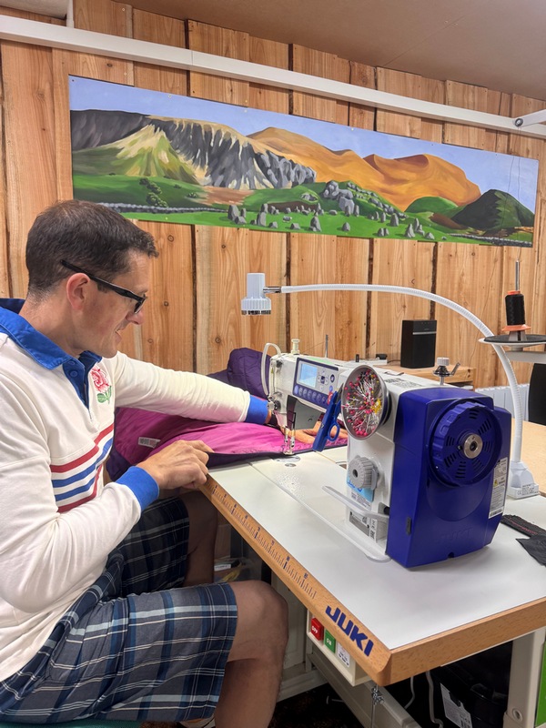 Man sitting at a sewing machine repairing a down jacket